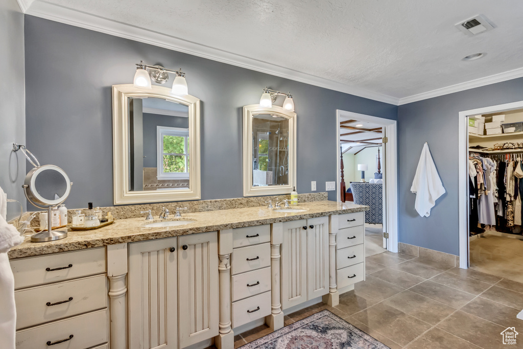 Bathroom featuring double vanity, visible vents, ornamental molding, and a sink