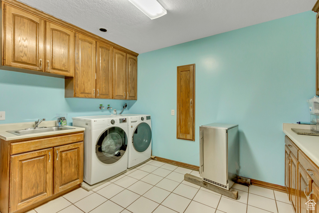 Clothes washing area with a sink, light tile patterned flooring, baseboards, separate washer and dryer, and cabinet space
