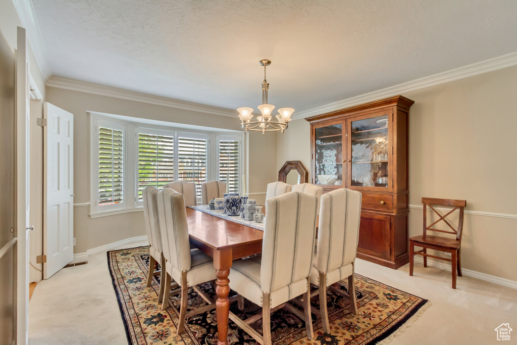 Dining room with baseboards, ornamental molding, light colored carpet, and a notable chandelier