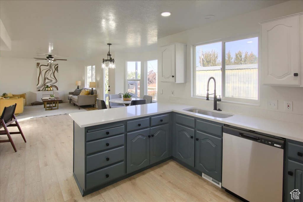 Kitchen with light wood finished floors, a peninsula, stainless steel dishwasher, white cabinets, and a sink
