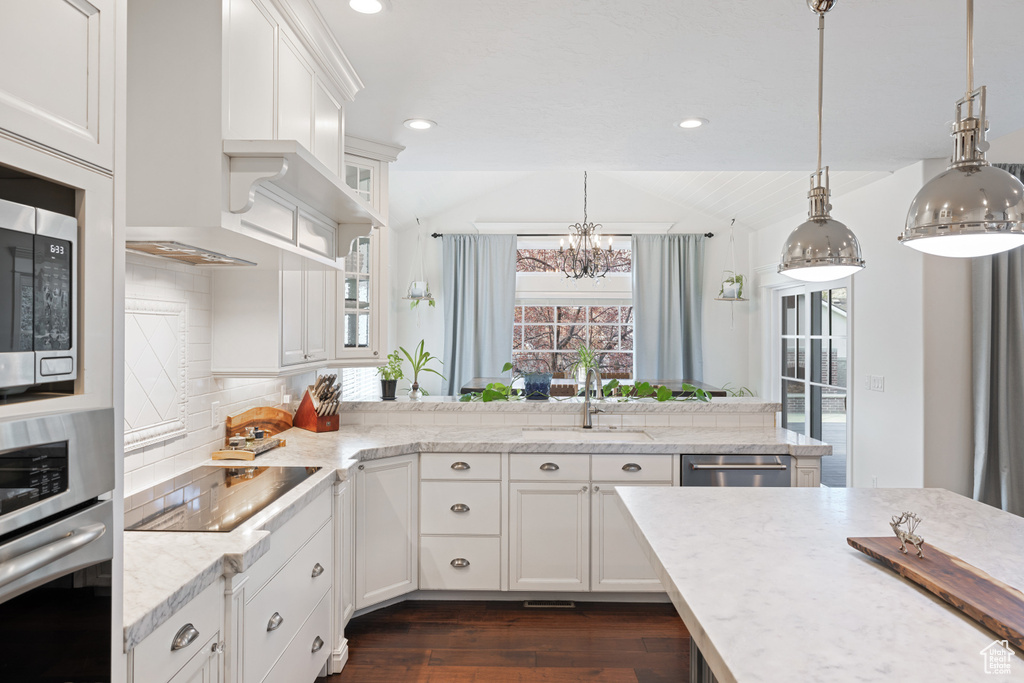 Kitchen with a sink, vaulted ceiling, a notable chandelier, dark wood-type flooring, and appliances with stainless steel finishes