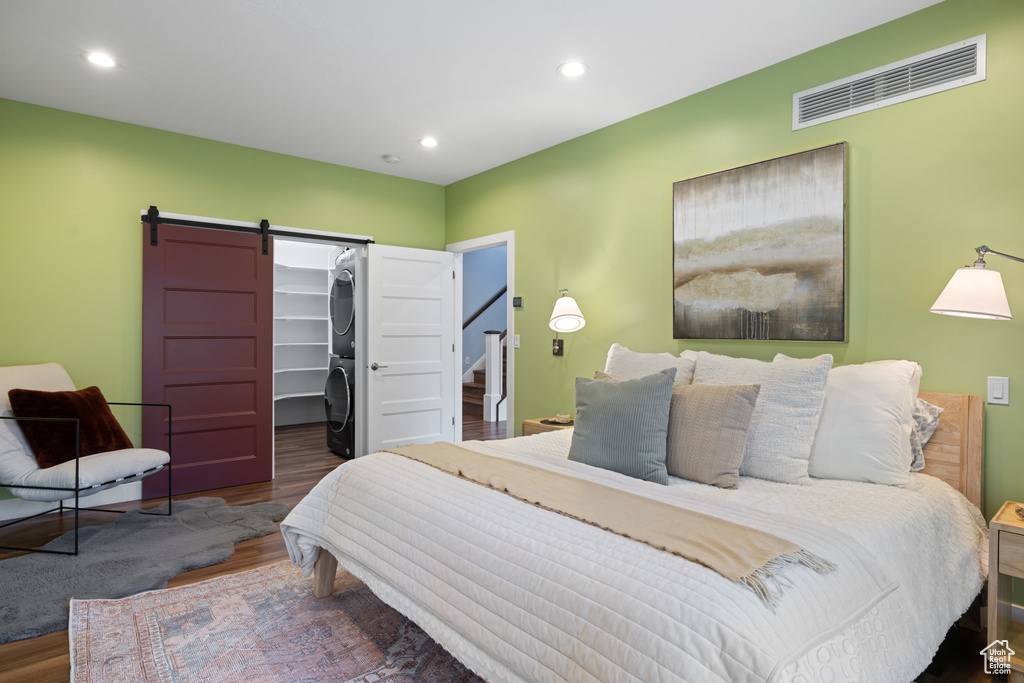 Bedroom with a barn door, wood finished floors, a spacious closet, stacked washer and dryer, and visible vents