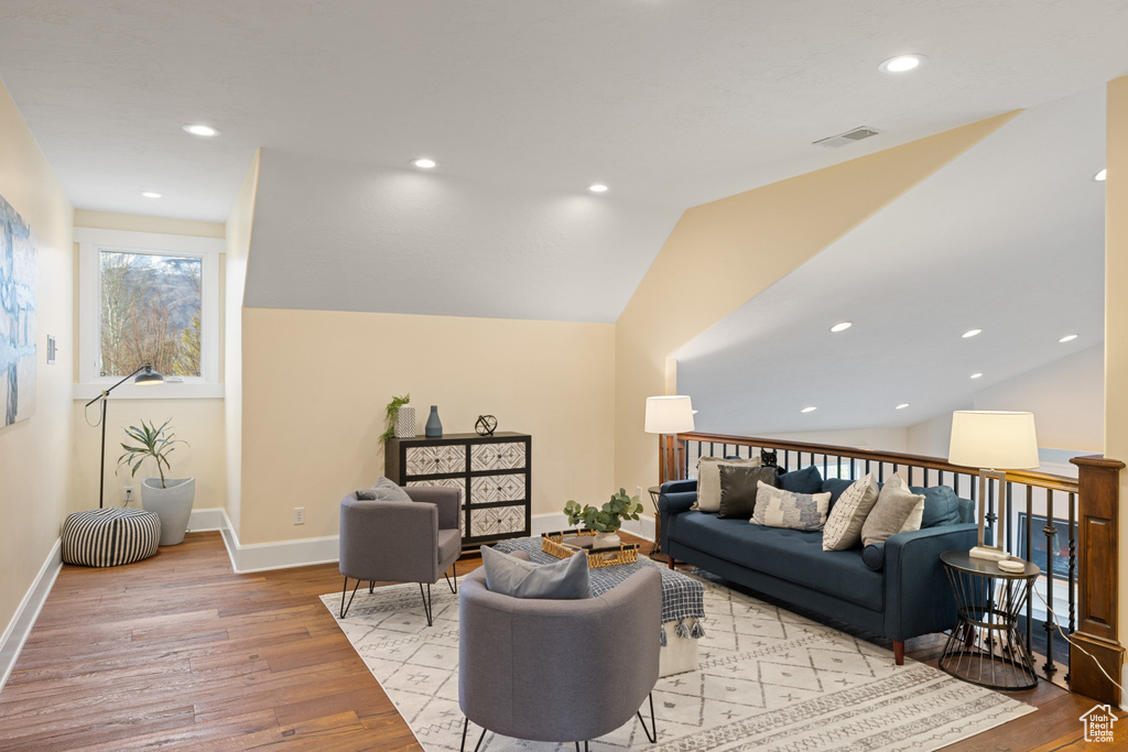Living area with light wood finished floors, baseboards, vaulted ceiling, and visible vents