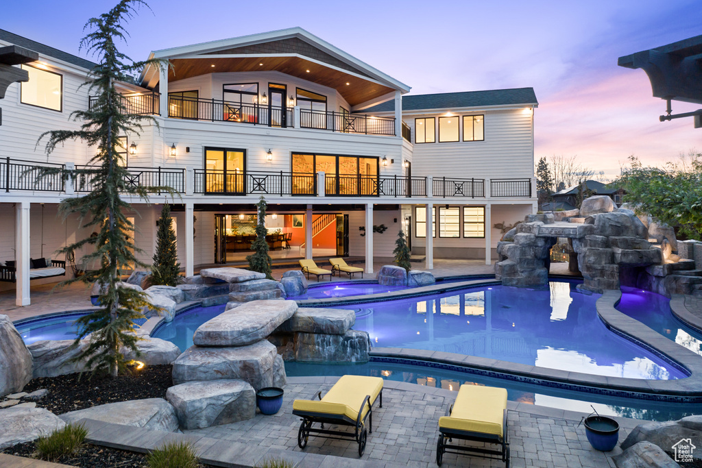 Back of property featuring an outdoor pool, a balcony, an outdoor hot tub, and a patio