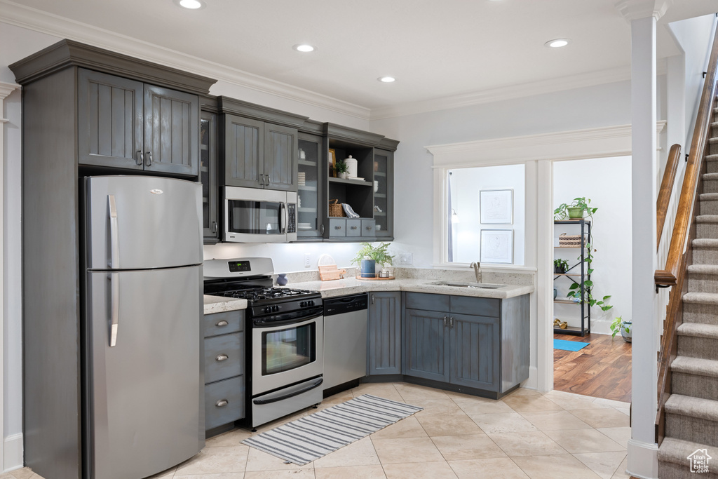 Kitchen featuring light stone counters, crown molding, a sink, glass insert cabinets, and appliances with stainless steel finishes