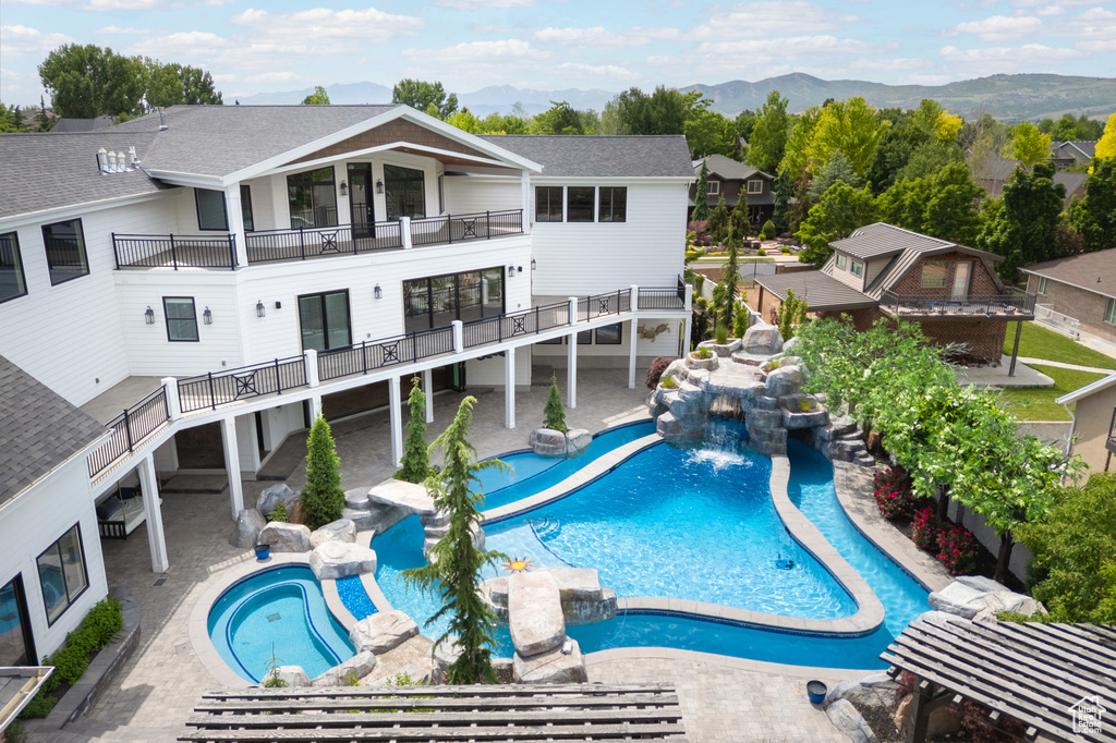 Rear view of house featuring a balcony, a mountain view, a pool with connected hot tub, a shingled roof, and a residential view