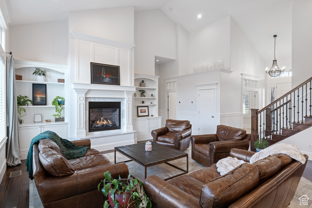 Living area with high vaulted ceiling, a glass covered fireplace, a chandelier, a wealth of natural light, and visible vents