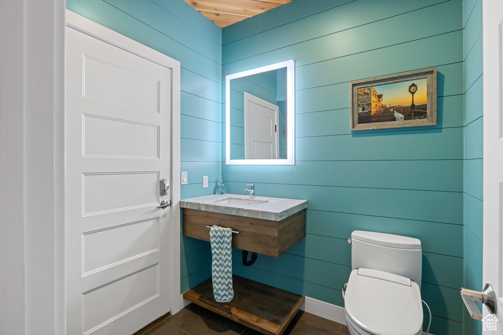 Half bathroom featuring toilet, wood walls, tile patterned flooring, and a sink