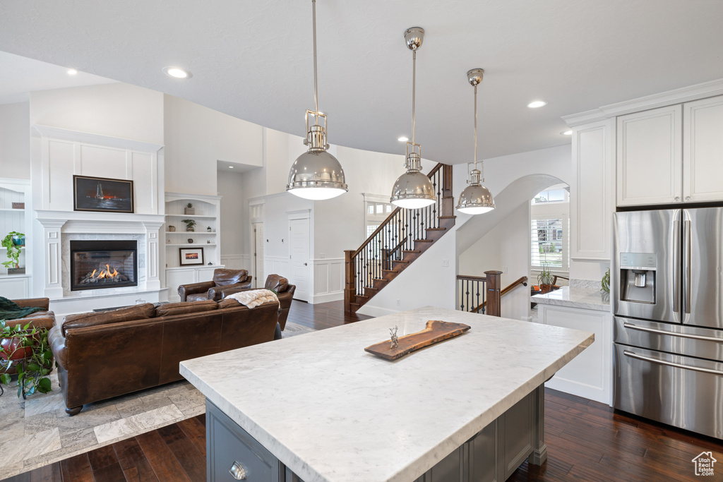 Kitchen with a glass covered fireplace, stainless steel fridge, arched walkways, white cabinetry, and dark wood-style floors