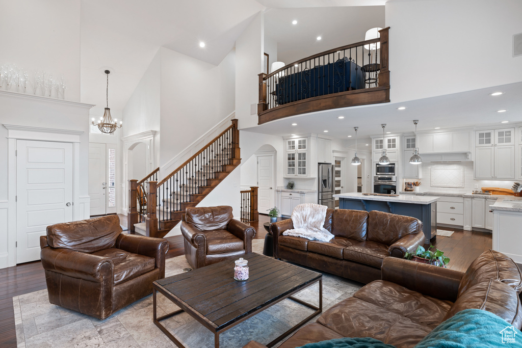Living area featuring stairway, wood finished floors, an inviting chandelier, a high ceiling, and recessed lighting