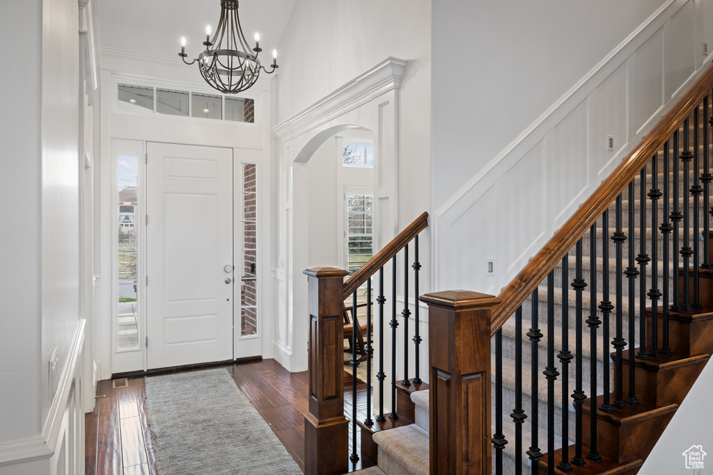 Entryway with dark wood-style floors, arched walkways, a notable chandelier, stairs, and a decorative wall
