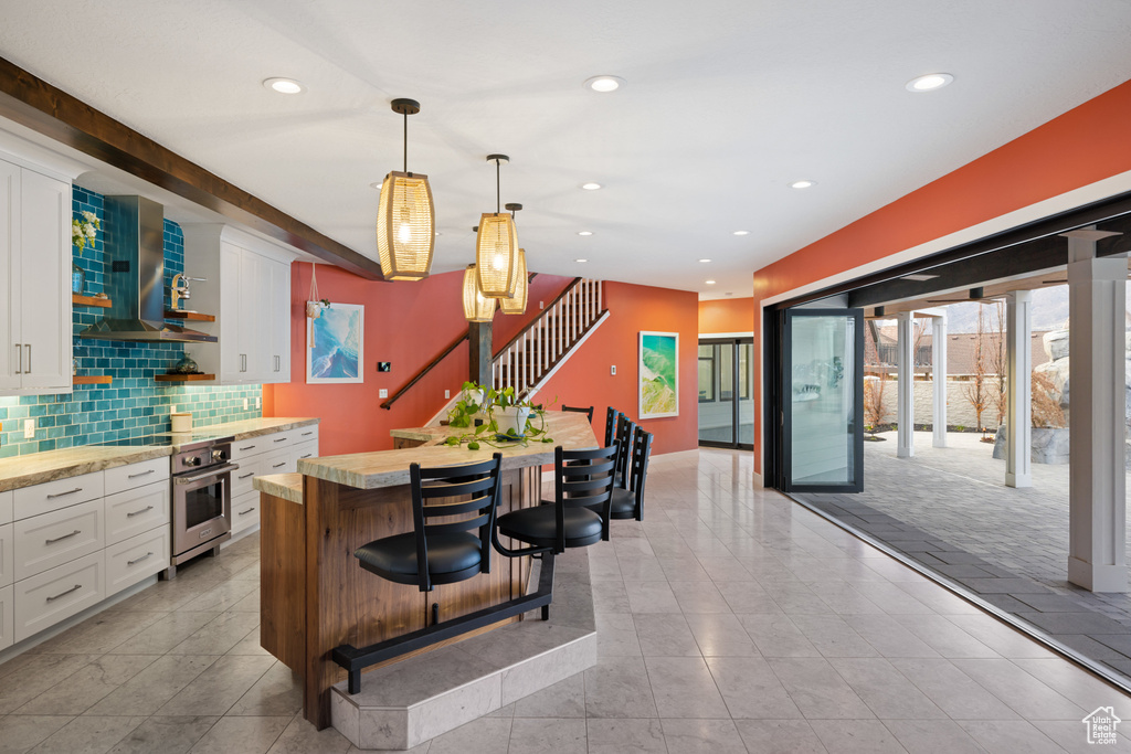 Kitchen with white cabinets, a center island, light countertops, and wall chimney range hood