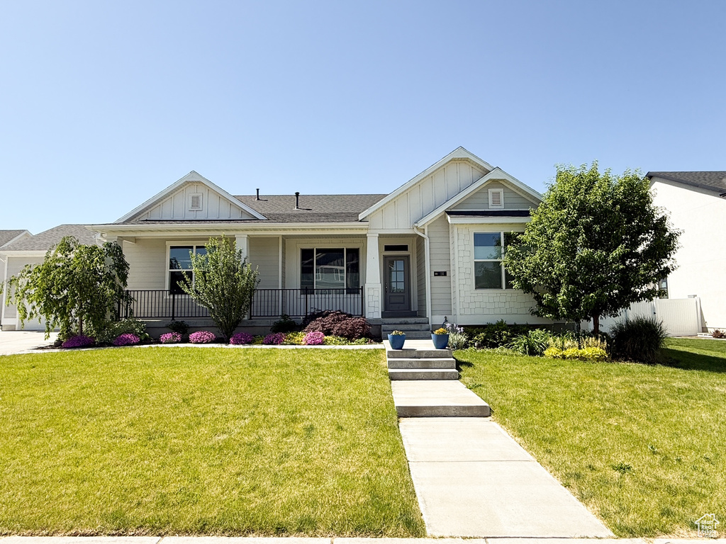 View of front of house featuring board and batten siding, covered porch, a front lawn, and an attached garage