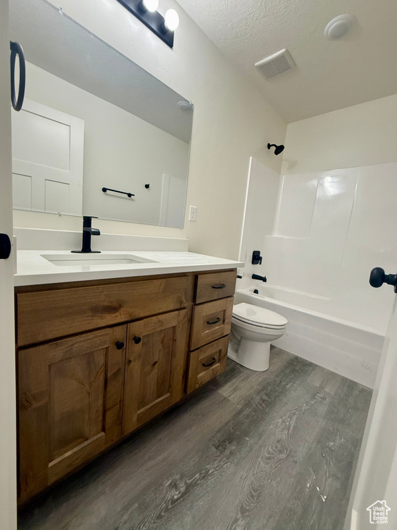 Full bathroom featuring wood finished floors, toilet, vanity, shower / bathtub combination, and a textured ceiling