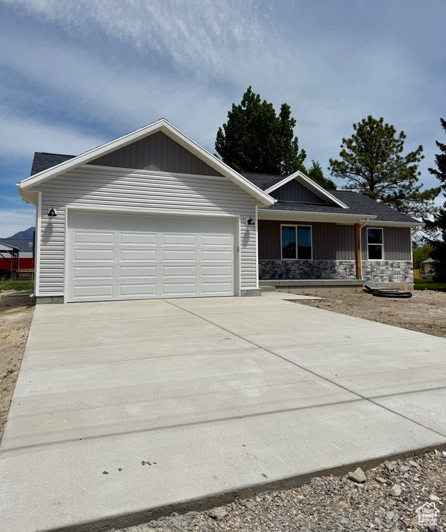 Single story home with an attached garage, concrete driveway, and stone siding