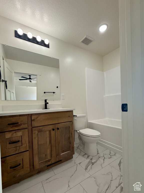 Bathroom featuring vanity, a ceiling fan, toilet, marble look tiles, and a textured ceiling