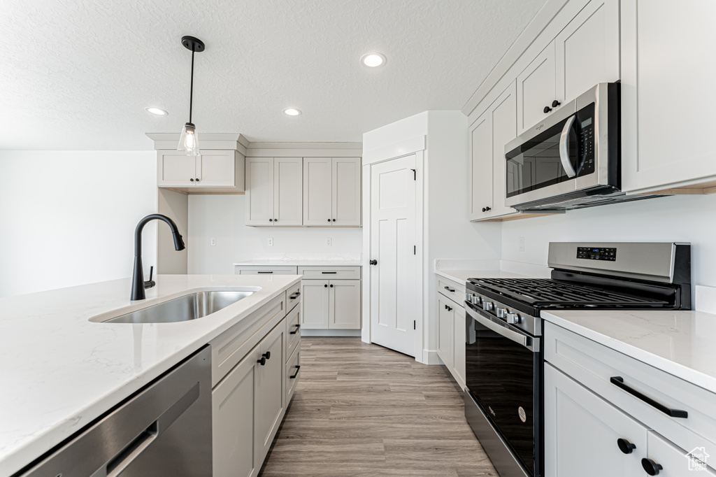 Kitchen with stainless steel appliances, recessed lighting, light wood-style floors, decorative light fixtures, and light stone countertops