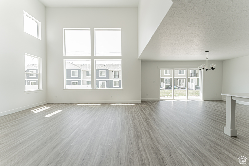 Unfurnished living room with a chandelier, light wood finished floors, and a towering ceiling