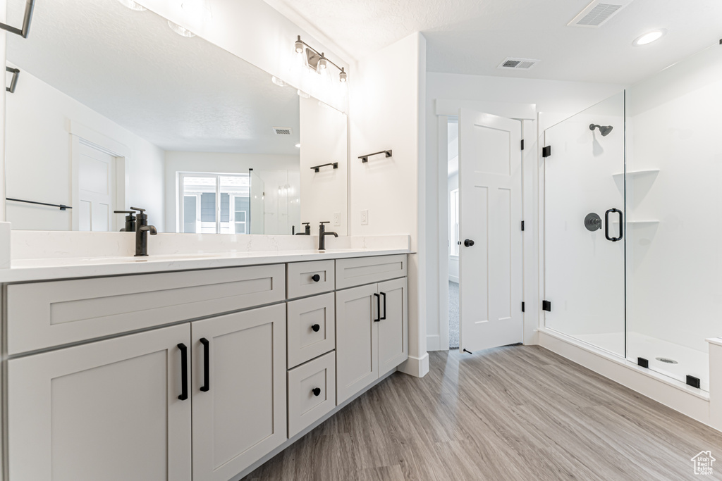 Full bath with wood finished floors, double vanity, and a shower stall
