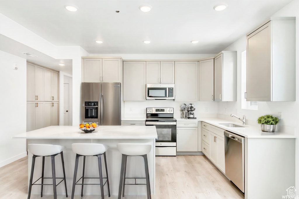 Kitchen with light wood-type flooring, a breakfast bar area, a sink, and appliances with stainless steel finishes