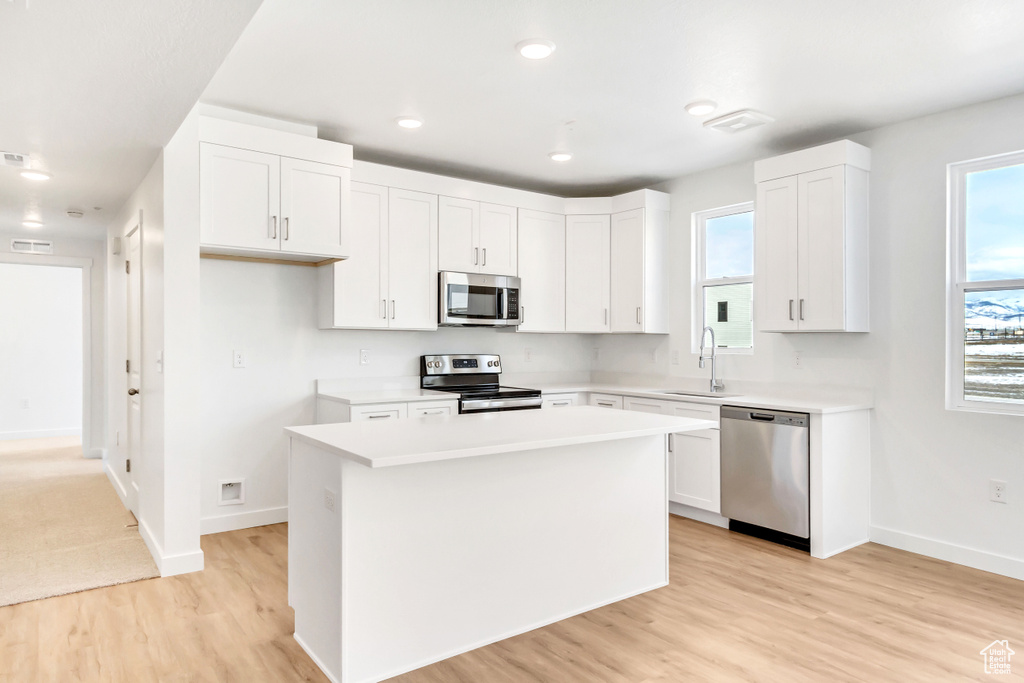 Kitchen featuring light wood finished floors, stainless steel appliances, a center island, visible vents, and baseboards