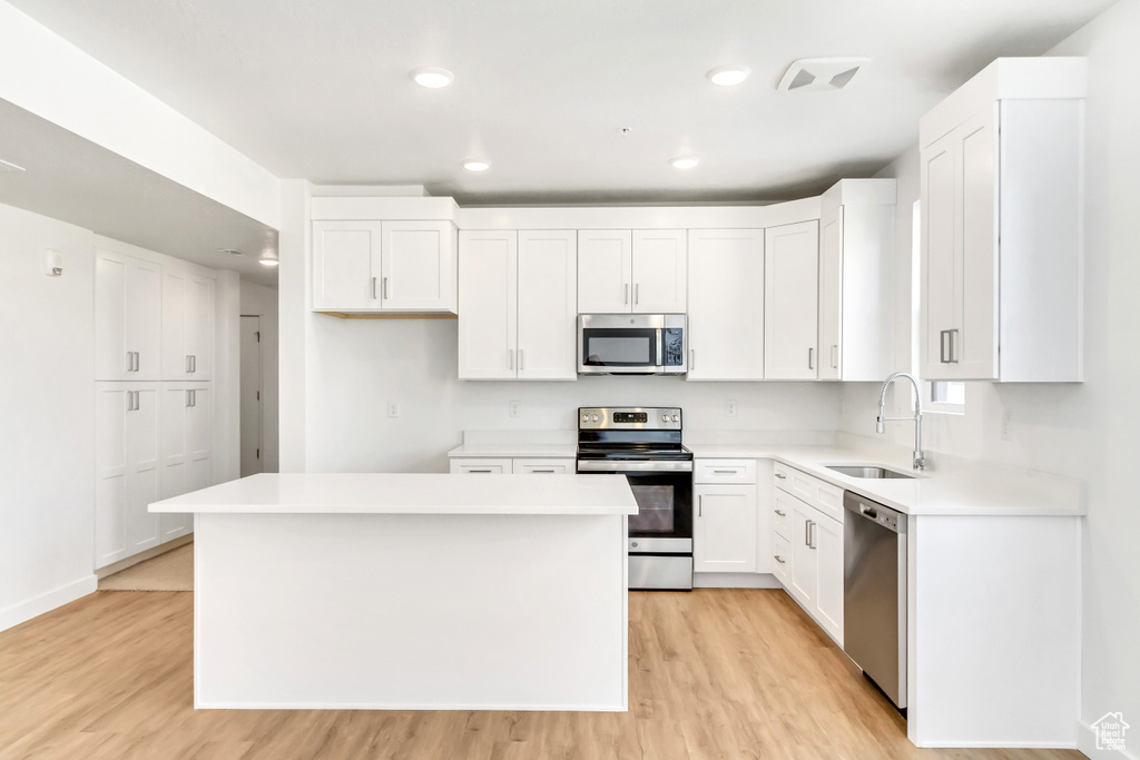 Kitchen with white cabinetry, light wood finished floors, stainless steel appliances, and a sink