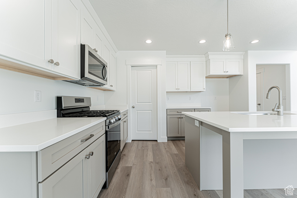 Kitchen featuring stainless steel appliances, recessed lighting, light wood finished floors, decorative light fixtures, and light countertops