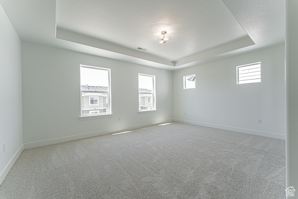 Carpeted empty room featuring a tray ceiling and baseboards