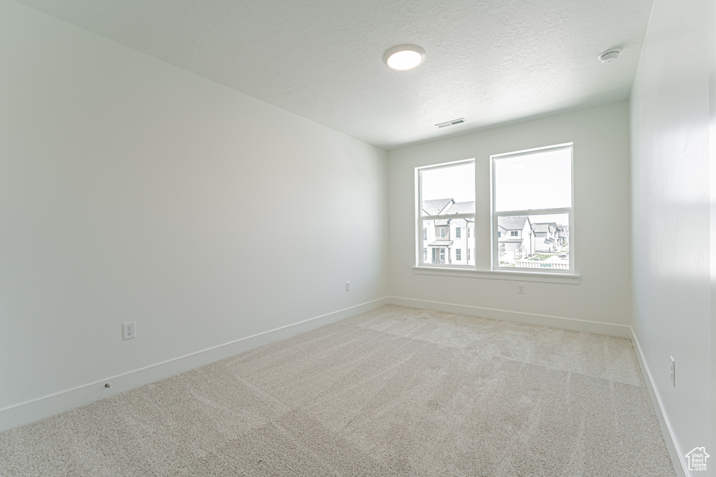 Empty room with a smoke detector, light carpet, and a textured ceiling