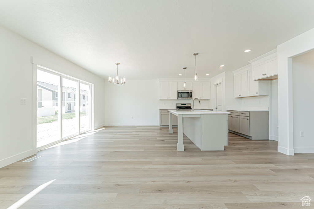 Kitchen featuring stainless steel microwave, a chandelier, a center island with sink, recessed lighting, and light countertops