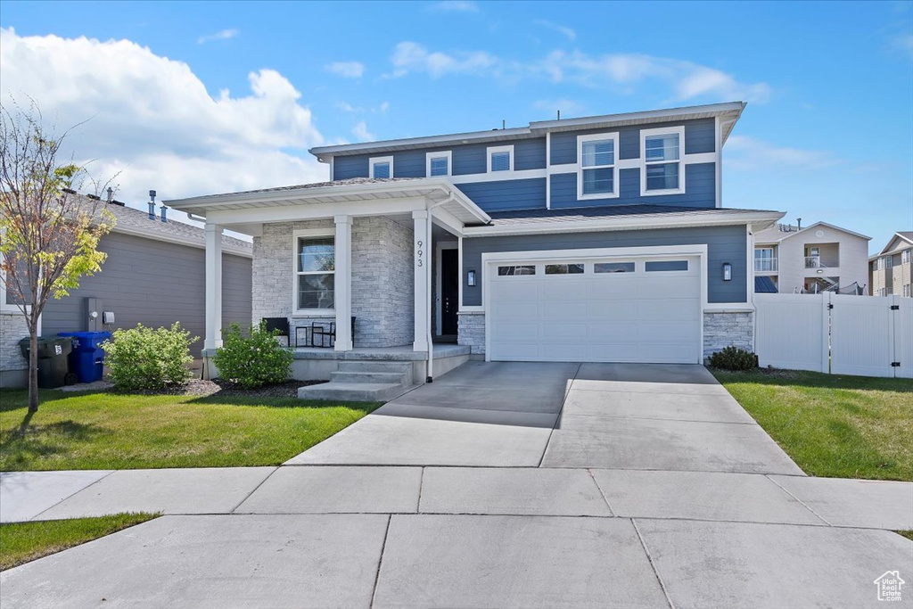 Prairie-style house featuring concrete driveway, a front lawn, stone siding, fence, and a porch