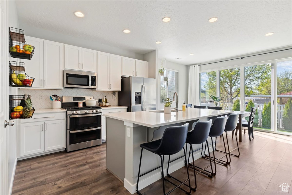 Kitchen featuring a kitchen island with sink, dark wood finished floors, recessed lighting, decorative backsplash, and appliances with stainless steel finishes