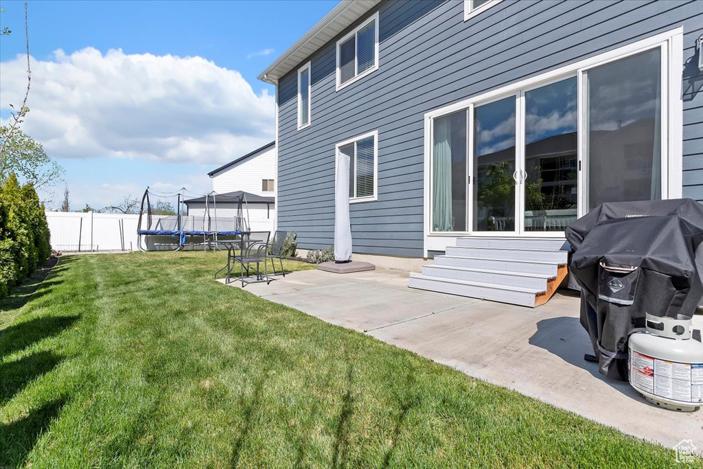 Back of property featuring a patio area, a trampoline, a lawn, fence, and entry steps