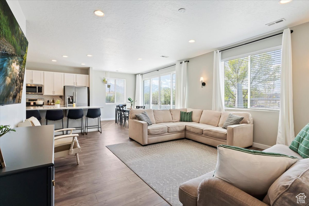 Living area with recessed lighting, wood finished floors, visible vents, and baseboards