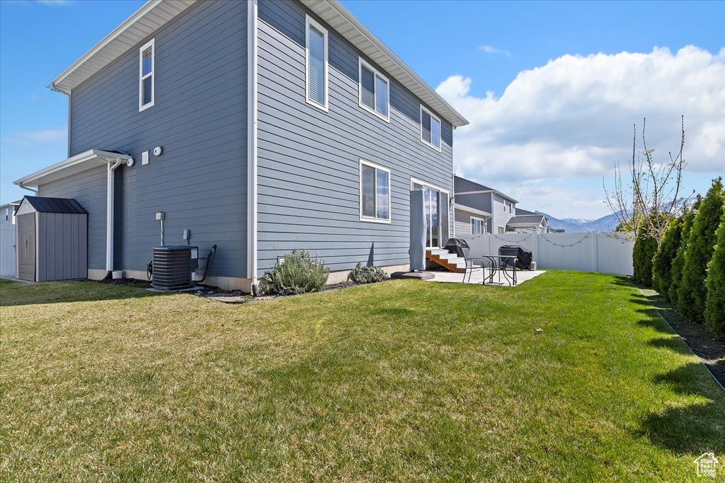 Back of property with a storage shed, a patio area, a lawn, and fence