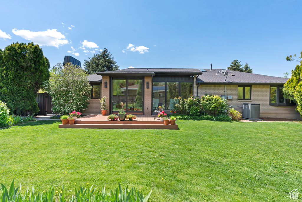 Rear view of house featuring central air condition unit, a wooden deck, a yard, and brick siding