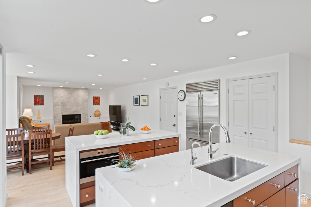 Kitchen featuring appliances with stainless steel finishes, a sink, brown cabinetry, an island with sink, and recessed lighting
