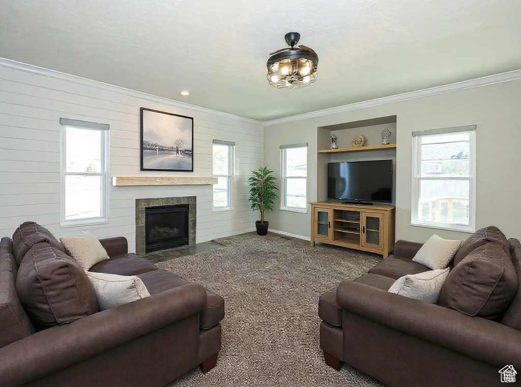 Living room with ornamental molding, plenty of natural light, carpet flooring, wood walls, and a fireplace