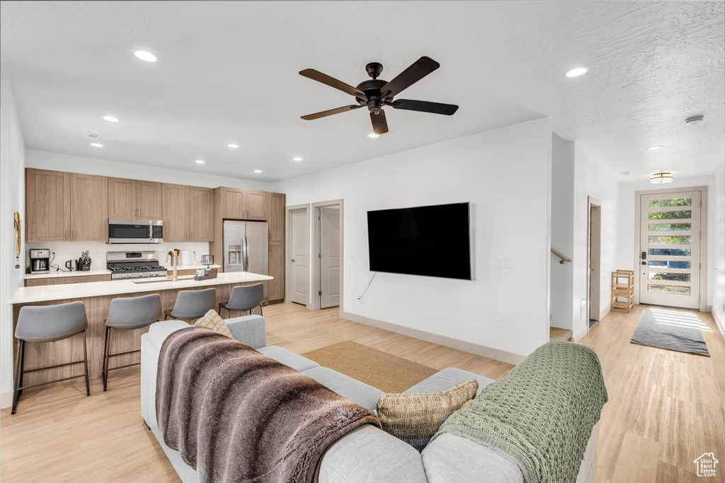Living room with ceiling fan, recessed lighting, baseboards, and light wood-style floors