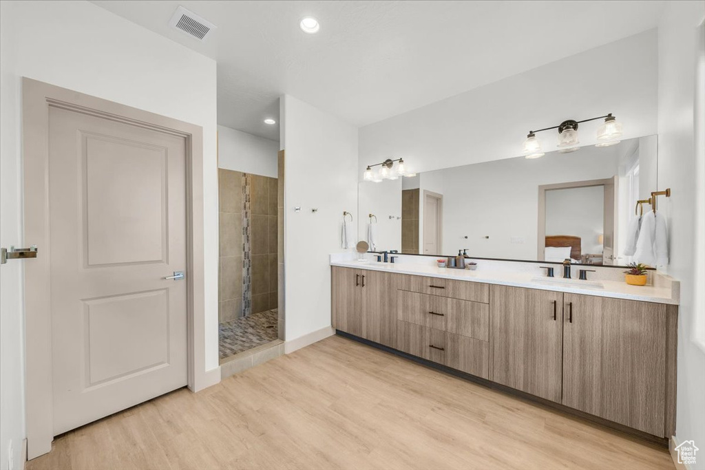 Full bathroom with a sink, double vanity, visible vents, wood finished floors, and tiled shower