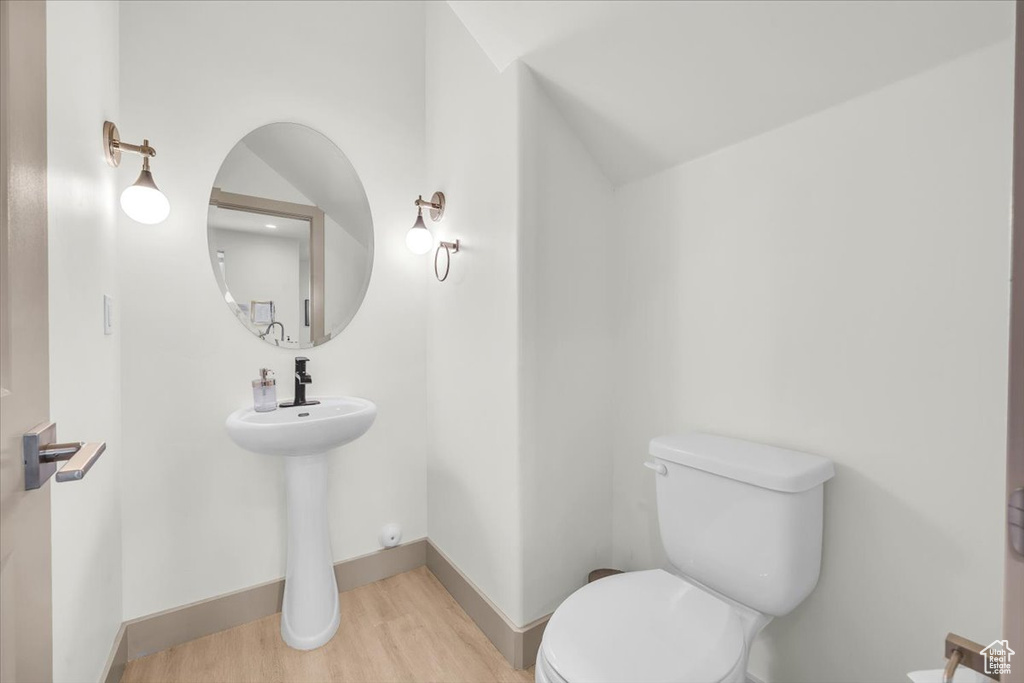 Half bathroom featuring wood finished floors, toilet, and baseboards