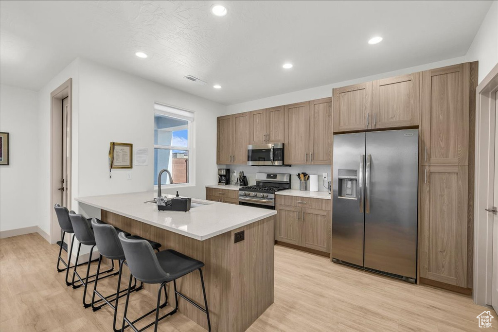 Kitchen with light wood finished floors, a kitchen bar, a sink, and stainless steel appliances