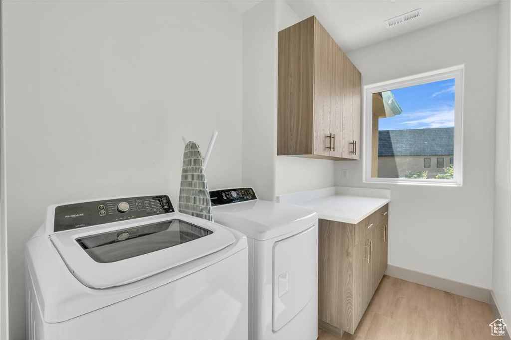 Washroom with cabinet space, independent washer and dryer, light wood-type flooring, visible vents, and baseboards