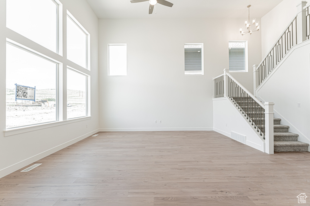 Unfurnished living room featuring stairs, ceiling fan, light wood finished floors, and a chandelier