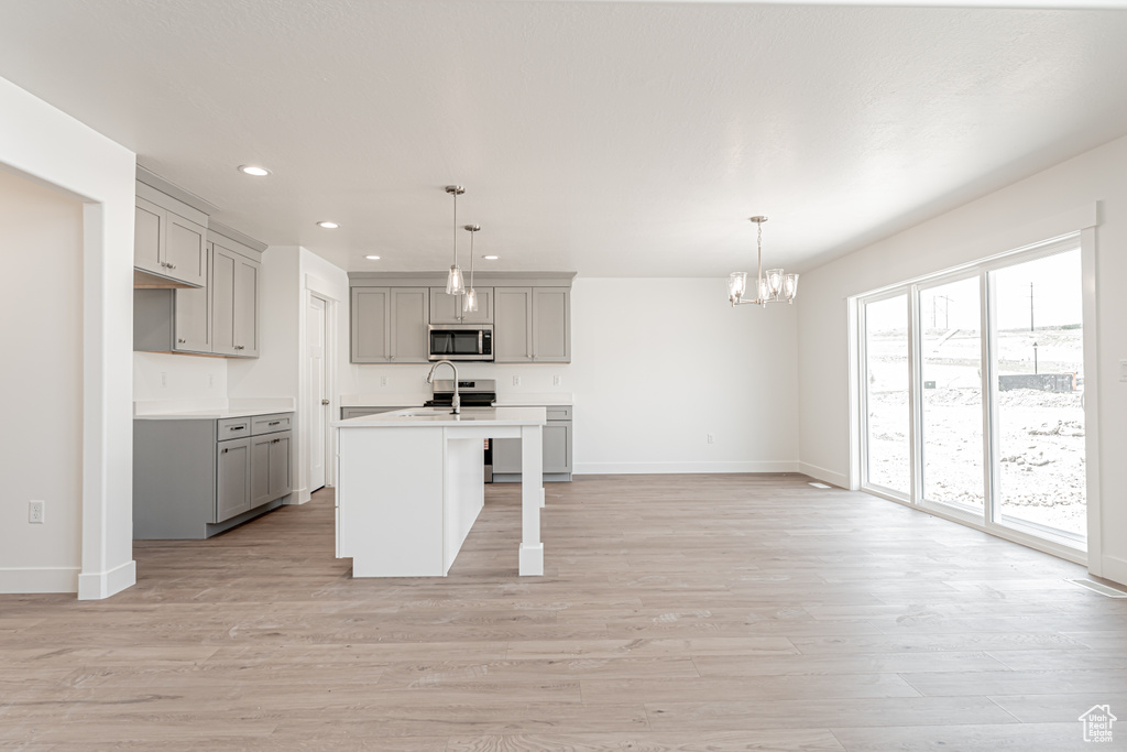 Kitchen featuring stainless steel microwave, gray cabinets, a chandelier, recessed lighting, and an island with sink