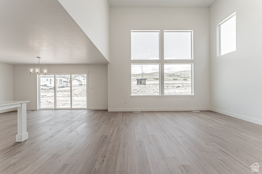 Unfurnished living room with a chandelier, light wood-style floors, and healthy amount of natural light