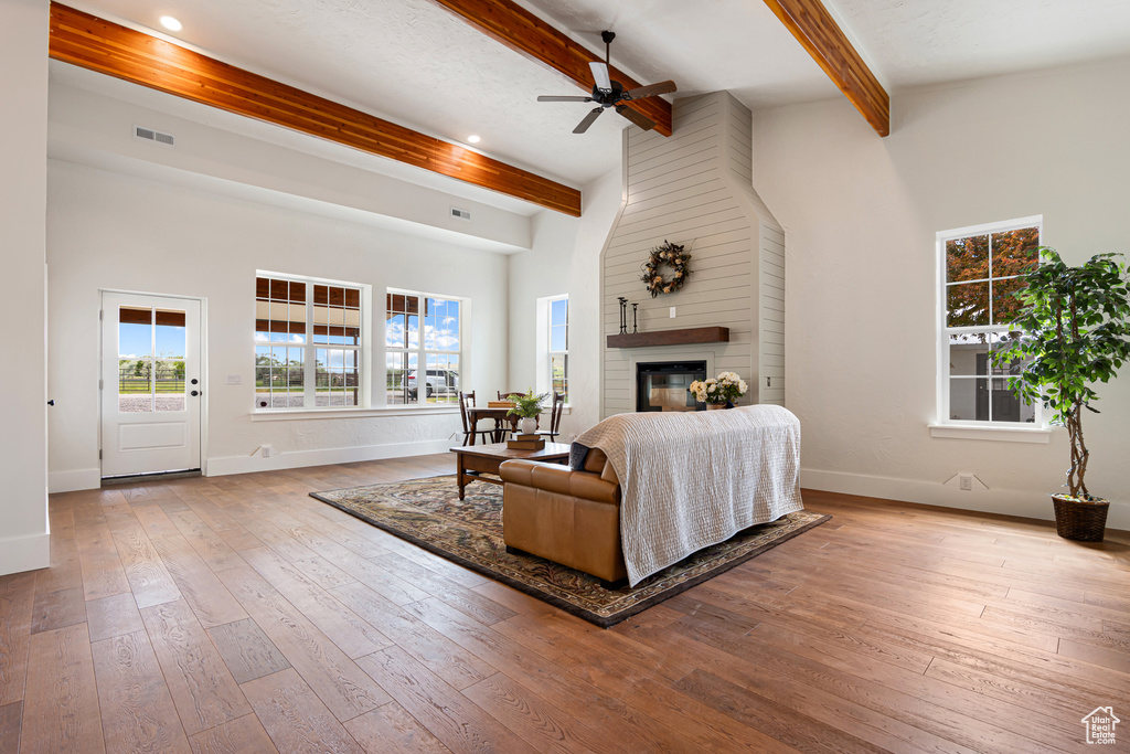 Living room featuring beamed ceiling, a ceiling fan, baseboards, hardwood / wood-style floors, and a large fireplace