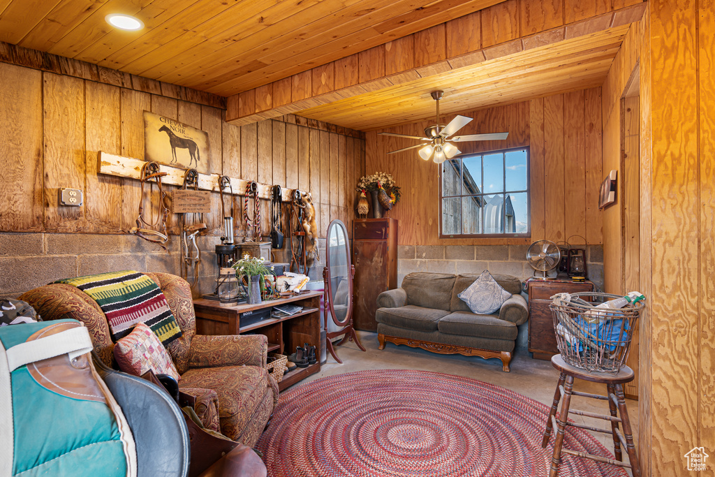 Living room featuring finished concrete flooring, wooden walls, wooden ceiling, and a ceiling fan