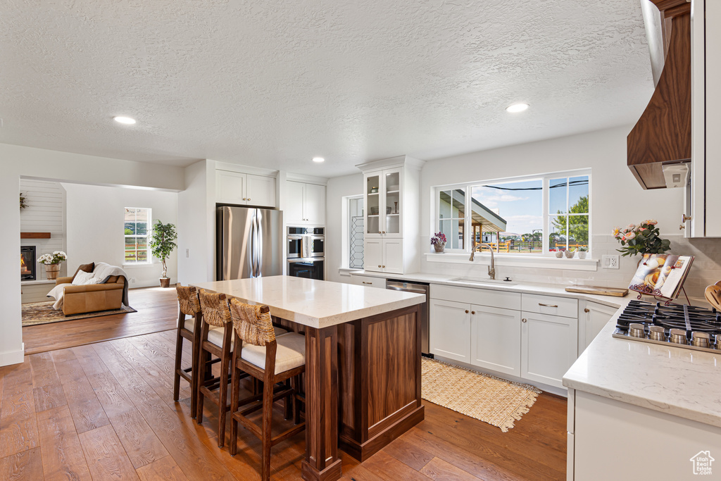 Kitchen featuring stainless steel appliances, a sink, wood-type flooring, a textured ceiling, and a center island