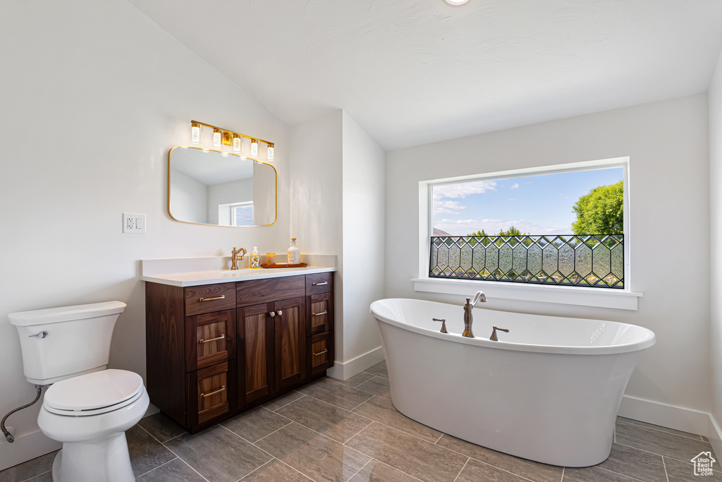 Bathroom featuring toilet, vanity, a soaking tub, and baseboards